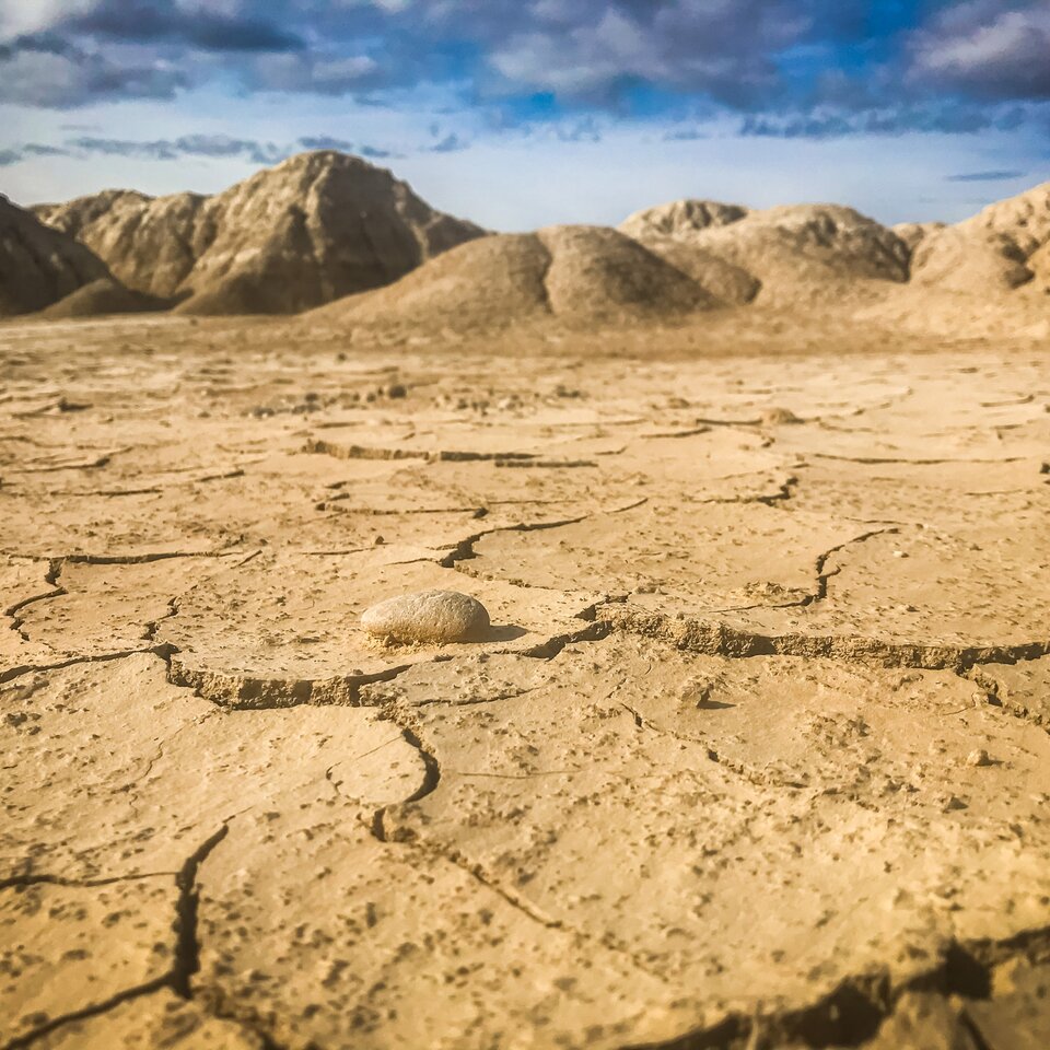 The picture from the travel report about a trip to the Pyrenees in a motorhome shows sandy-dry ground with cracks, with hills visible in the background. 