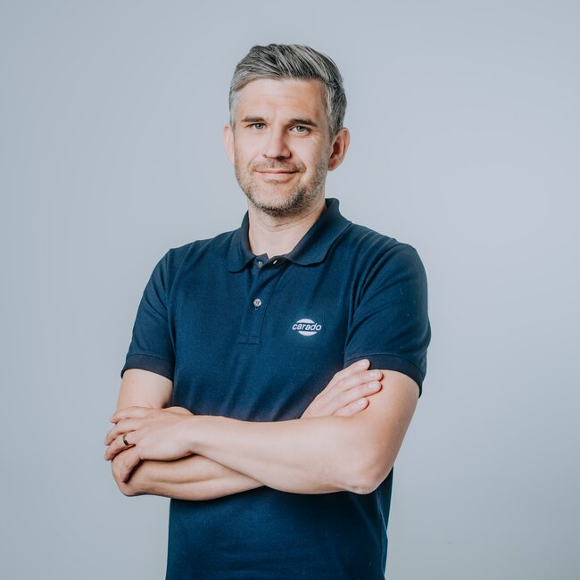 Man in a Carado polo shirt with folded arms against a grey background