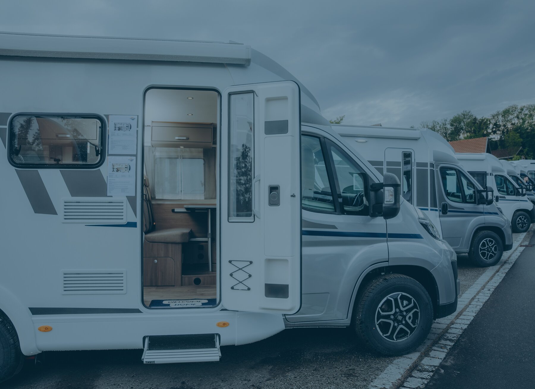 Camping-car Carado sur une aire de stationnement, porte cellule ouverte, avec vue sur l’intérieur et d’autres camping-cars à l’arrière-plan