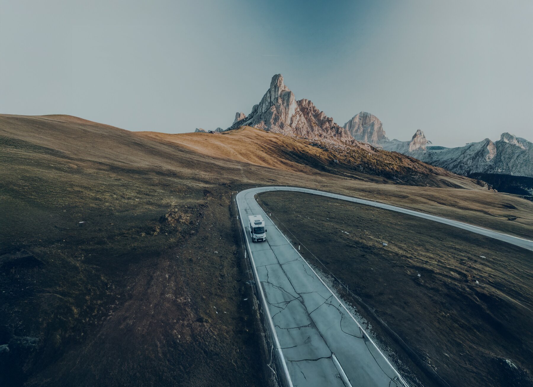 Carado motorhome on a winding mountain road in front of rocky peaks, aerial view