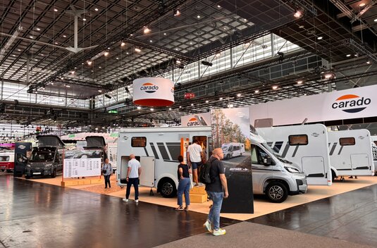 Carado Wohnmobile auf Messestand in großer Halle, Besucher besichtigen teilintegrierte Modelle