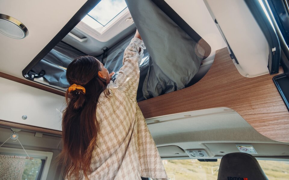 Person opening the roof bed in a Carado motorhome with a view of the roof window