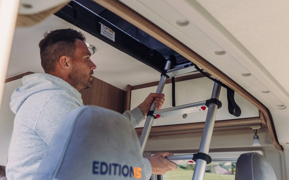 A man climbs the ladder inside the Carado motorhome to reach the drop-down bed.