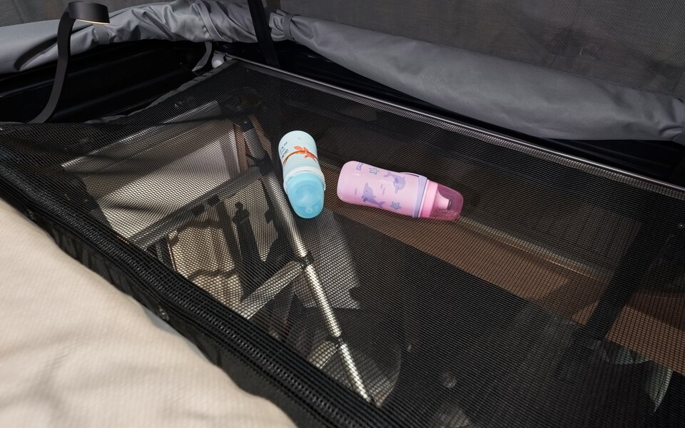 Storage space in the pop-up roof of a Carado motorhome with a net shelf, two water bottles and a folded frame