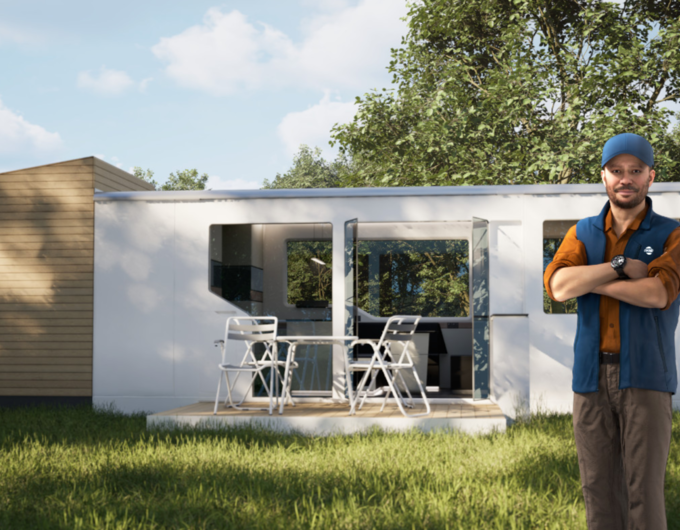 Mann vor modernem Tiny House mit Terrasse, Tisch und Stühlen auf einer Wiese
