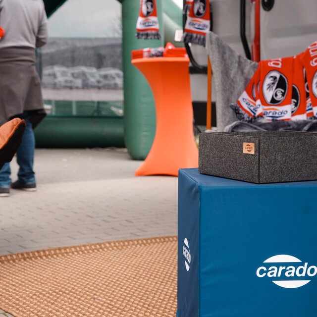 Carado motorhome with camping chairs, cushions and fan scarves in front of the vehicle at an event