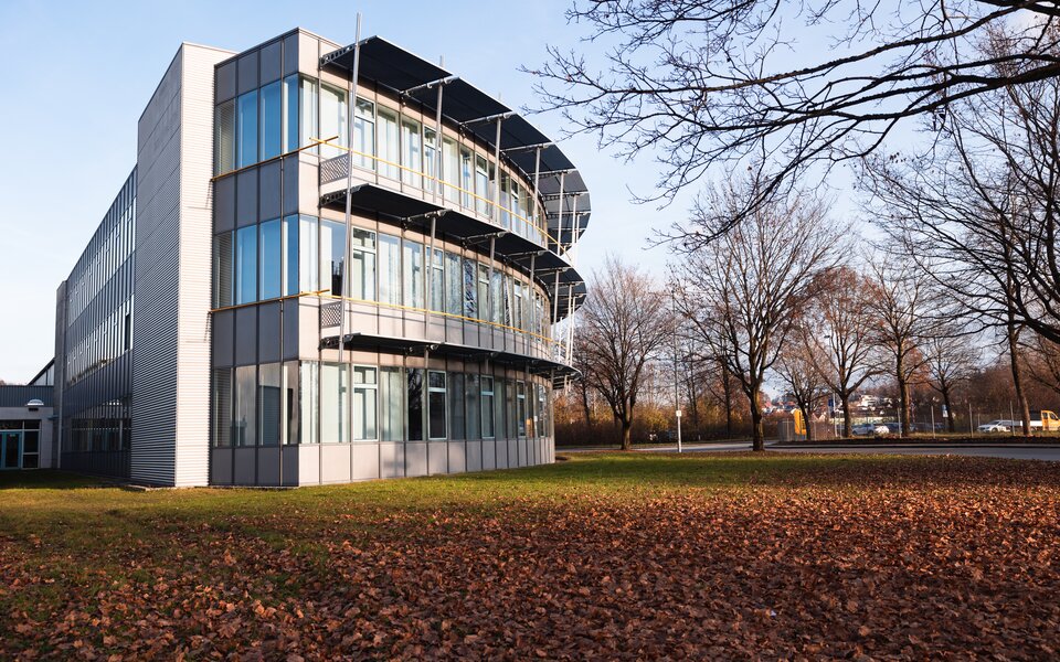 Modern office building with a glass façade, balconies and an autumn meadow covered in leaves
