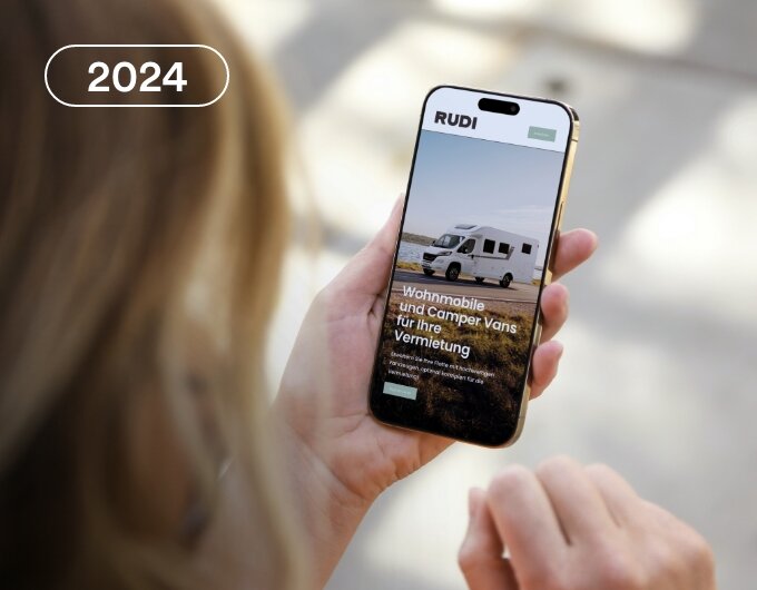 Person holding a smartphone displaying a website for motorhome and camper van rentals, with an image of a white camper van on the screen