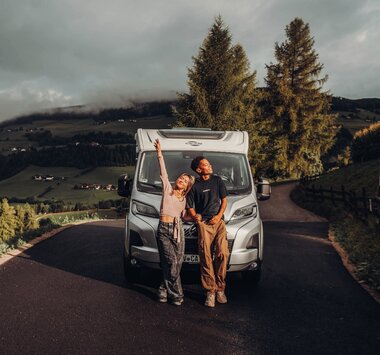 Two people standing in front of a Carado motorhome on a mountain road