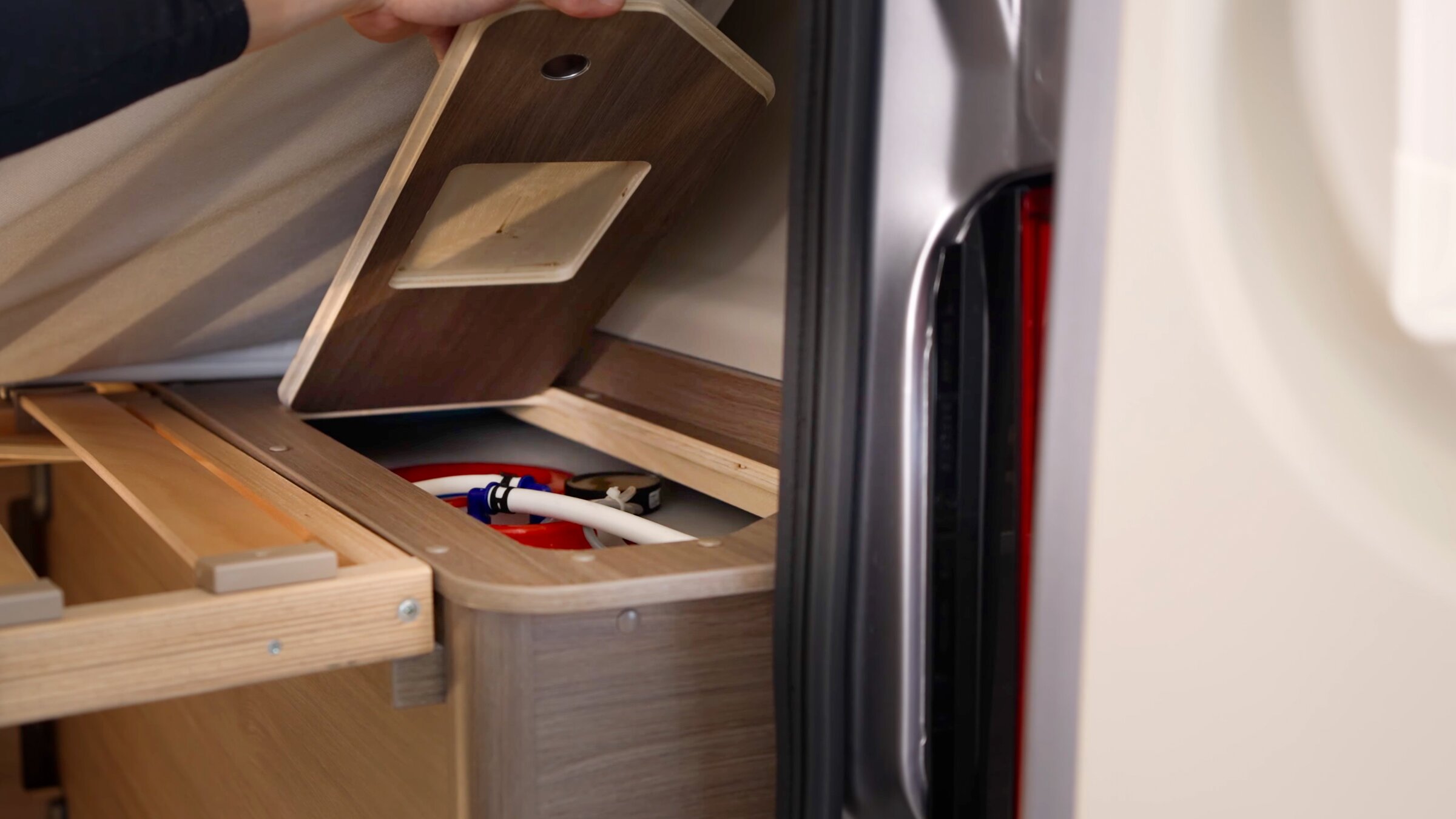 Stauraumfach im Carado Wohnmobil unter angehobener Abdeckung mit sichtbaren Anschlüssen und Holzrahmen