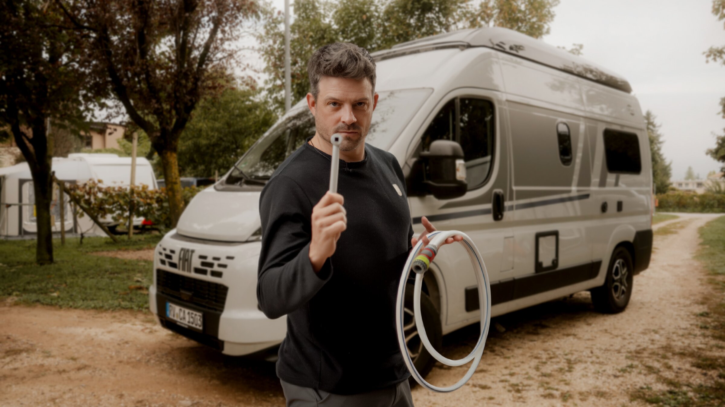 Person mit Schlauch und Anschluss vor Carado Wohnmobil auf Campingplatz