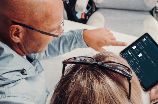Two people are viewing the Carado needs calculator on a tablet inside the motorhome