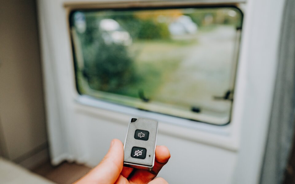 Hand holding a remote control in front of the motorhome window, inside the vehicle