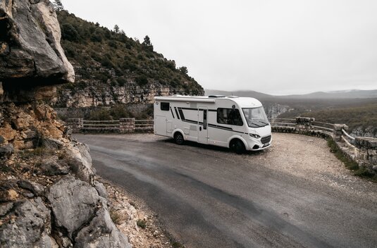 Carado motorhome on a mountain road with hairpin bends, beside a cliff with a view over the valley