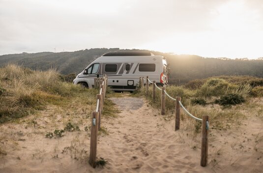 Carado motorhome on a sandy track between dunes, side view in the low evening sun