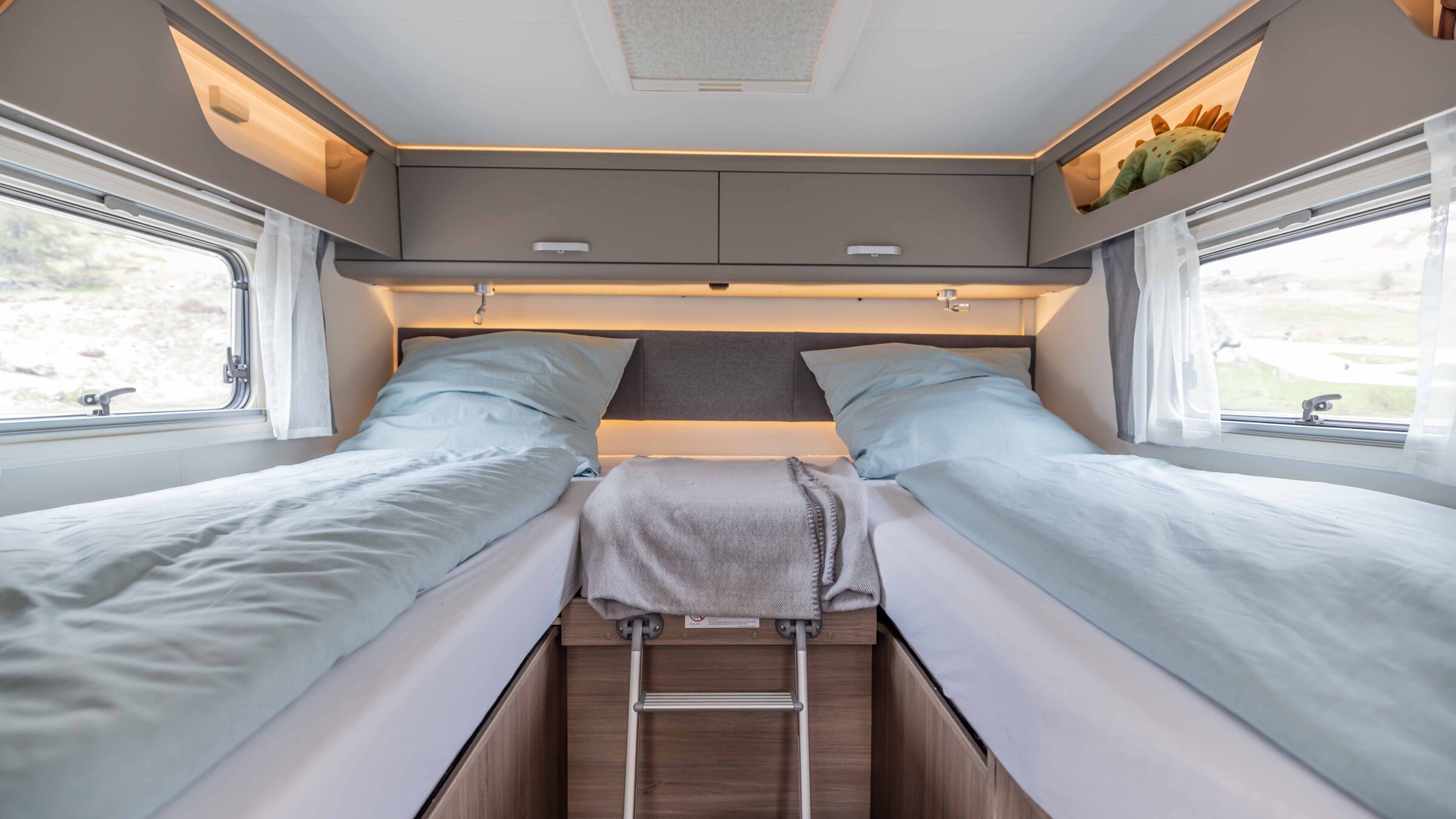 Sleeping area in the Carado motorhome with two single beds, a ladder, overhead lockers and side windows