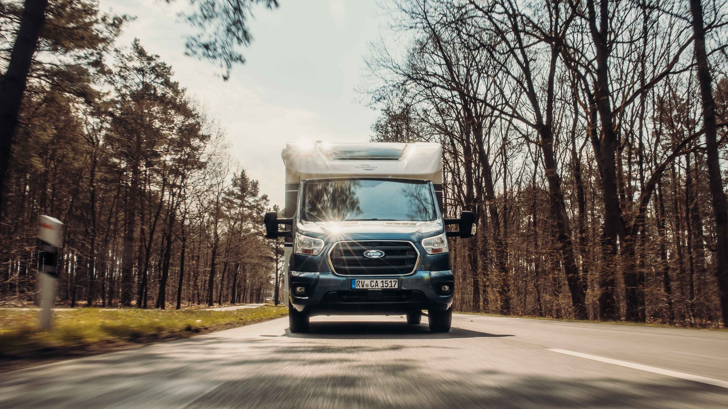 Carado Wohnmobil frontal auf Landstraße durch Wald, mit Bewegungsunschärfe