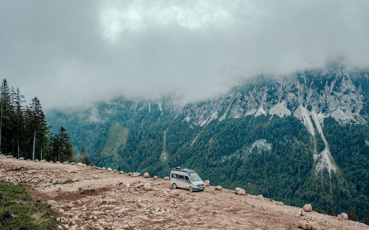 Carado motorhome on a rocky mountain plateau, with wooded mountains and low-hanging clouds in the background