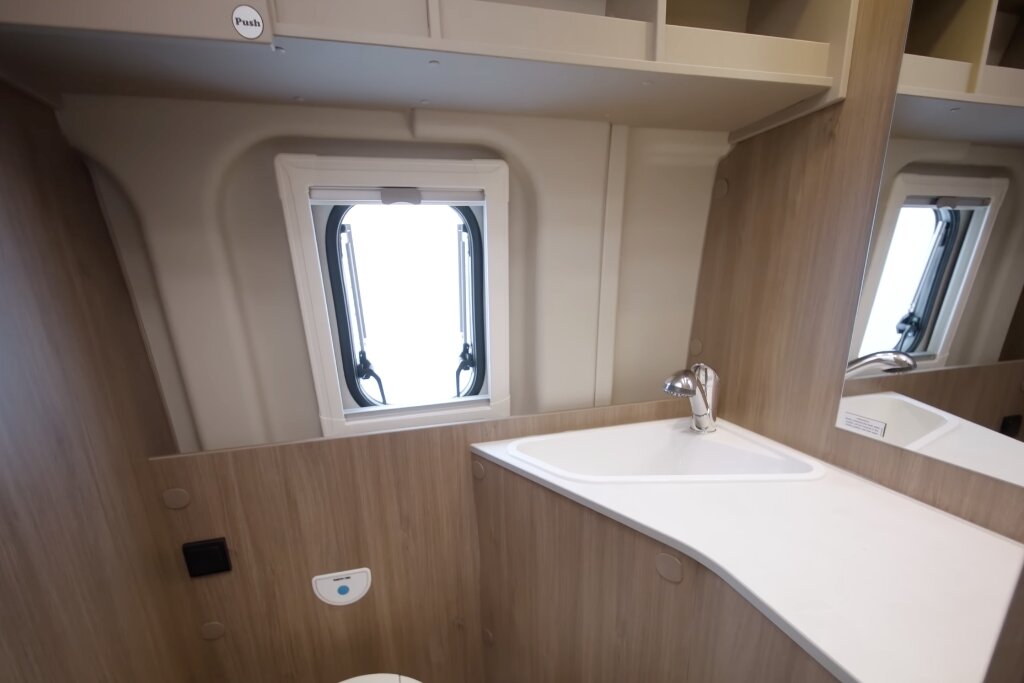 Bathroom in the Carado motorhome with washbasin, mirror, window and wood décor