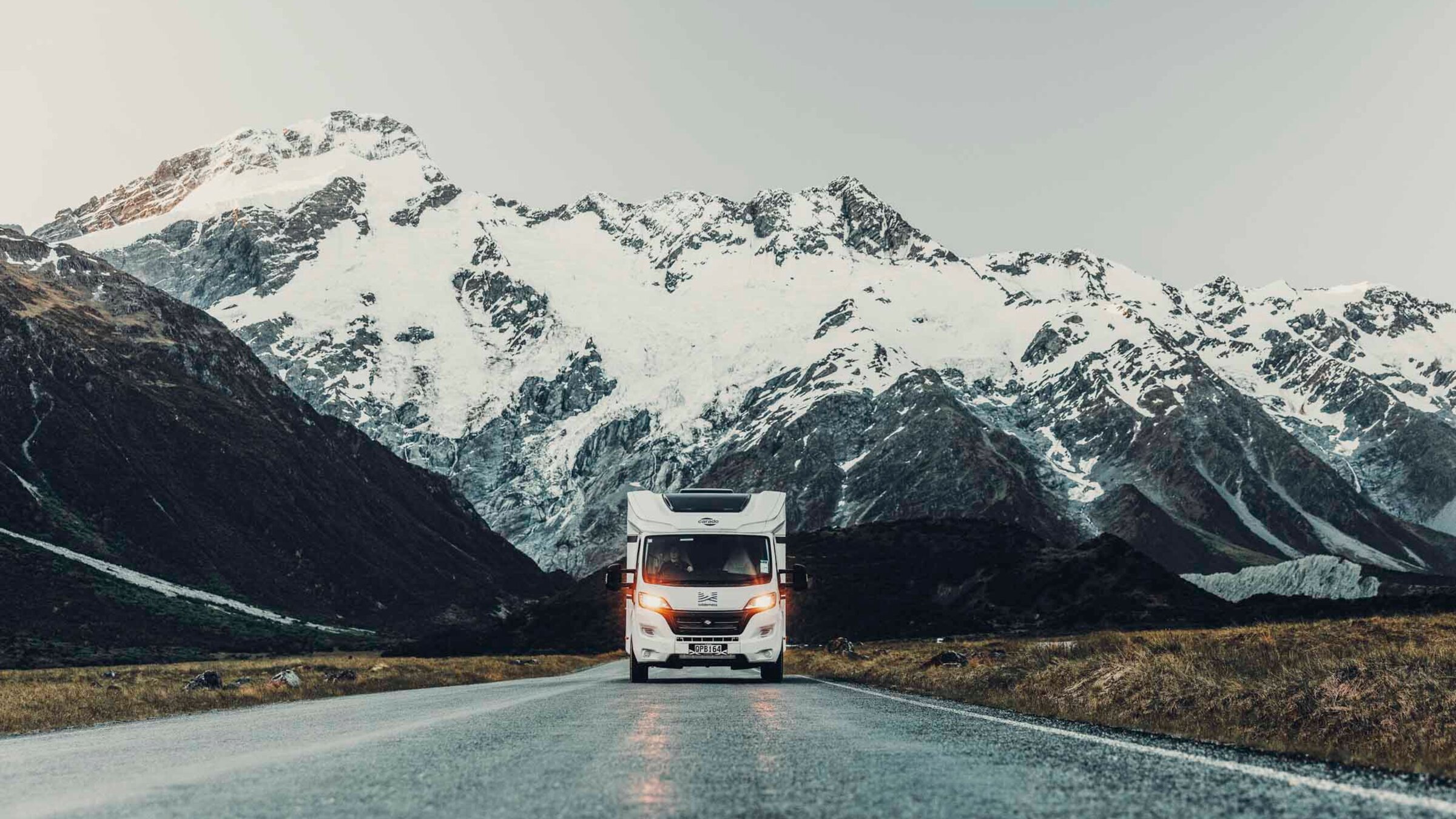 Carado motorhome from the front on a wet road, with snow-covered mountains in the background