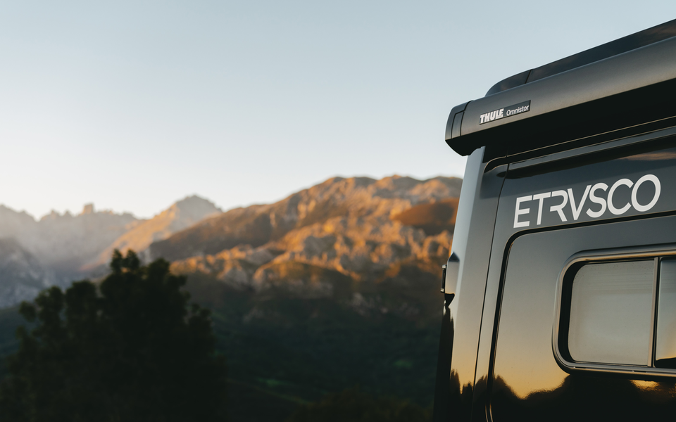 Rear view of an Etrusco campervan in front of a picturesque mountain backdrop at sunrise, ideal for camping in nature.