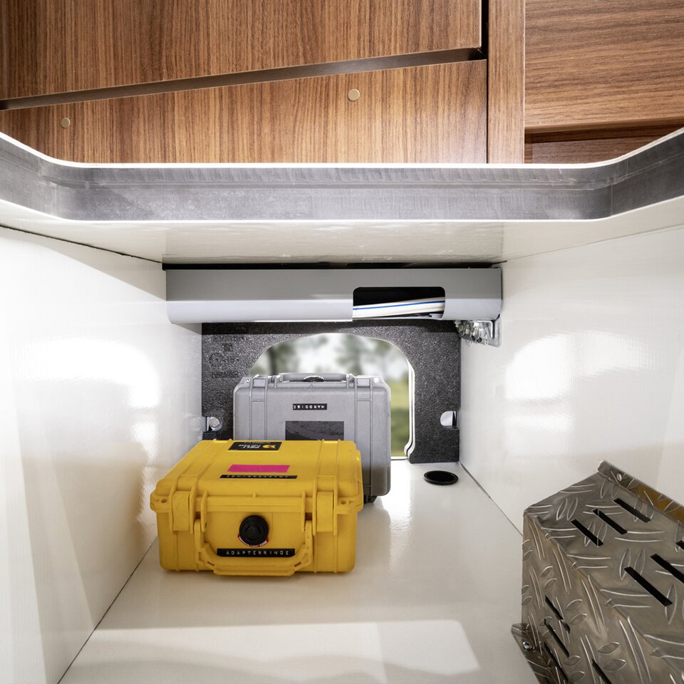 A yellow and a grey accessory case with black and white lettering in the Mercedes camper van, with cables, an aperture and against woodern decor.
