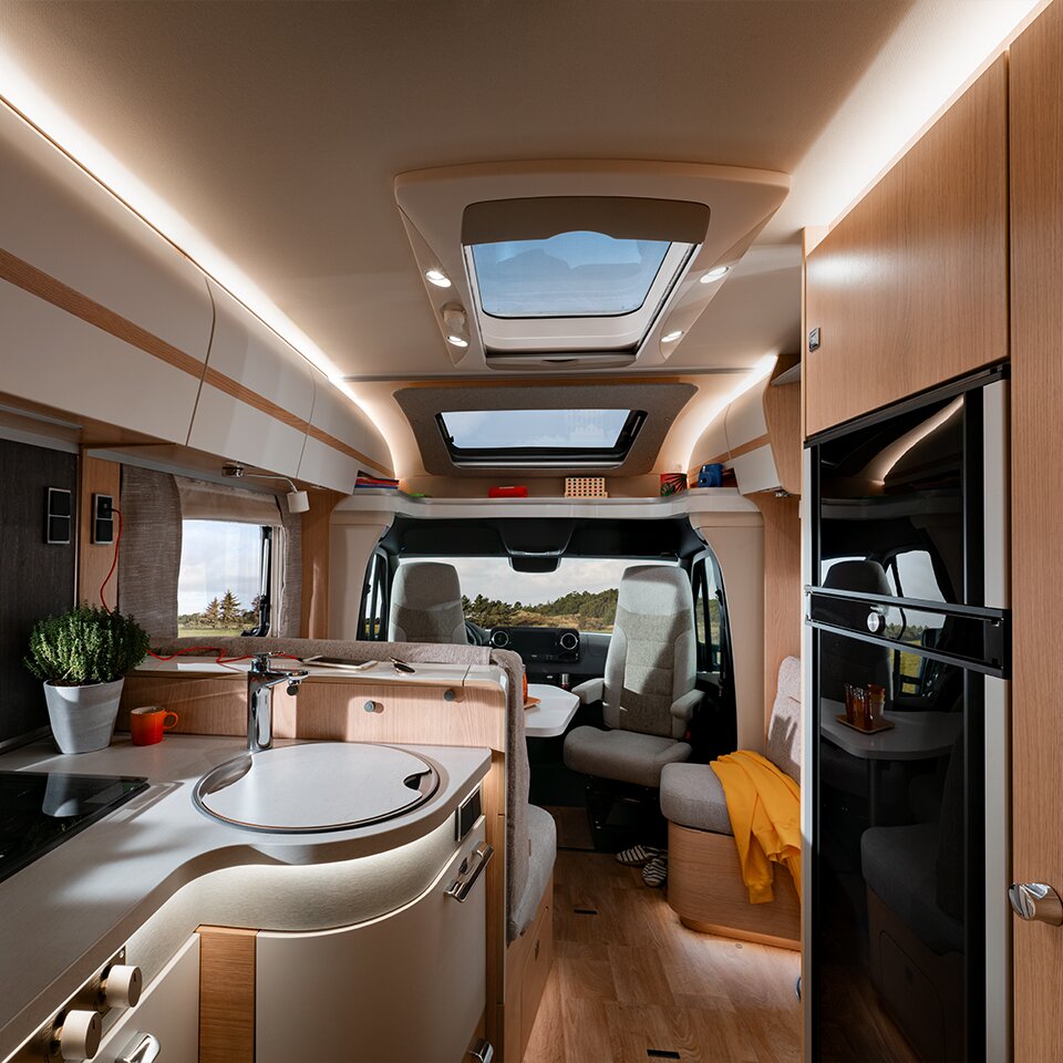 View of the kitchen and seating area of the HYMER B-Class MasterLine T, nature can be seen through the windscreen. A yellow jacket lies on the bench.