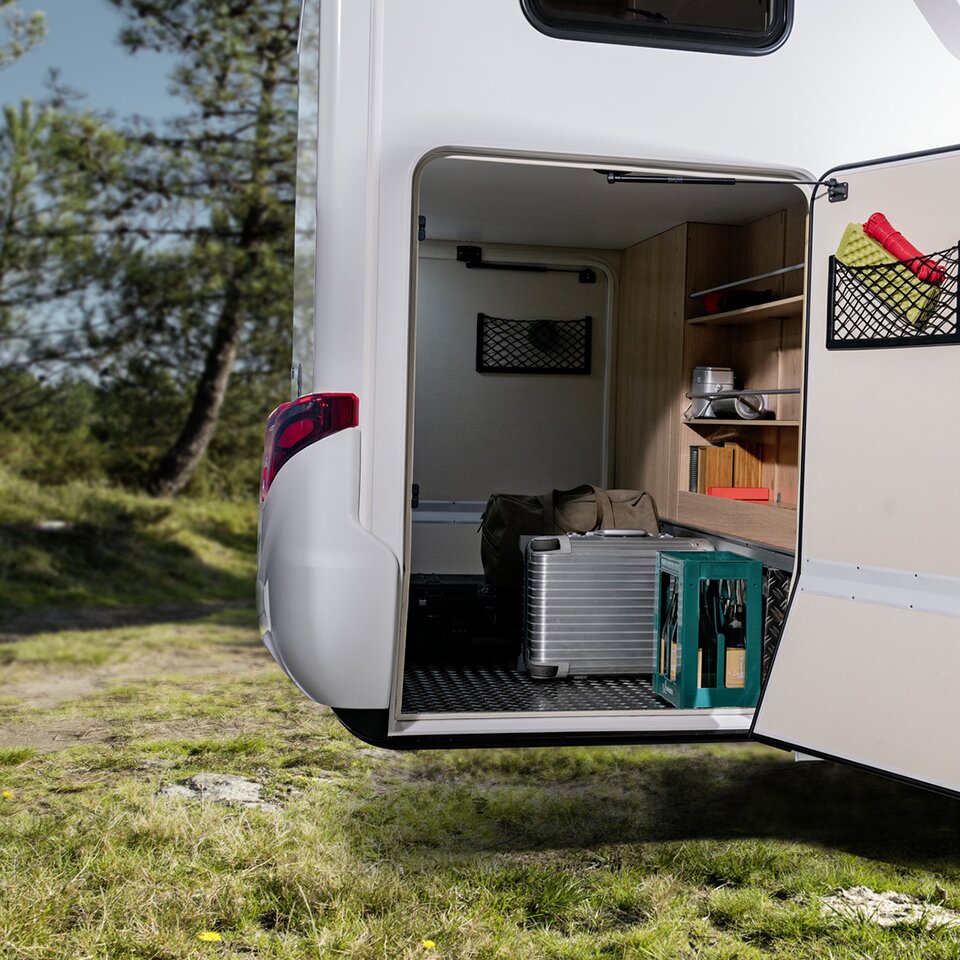 The garage of the Mercedes HYMER B-Class Modern Comfort T is open on one side and contains suitcases, a bag, a drinks crate and other accessories.