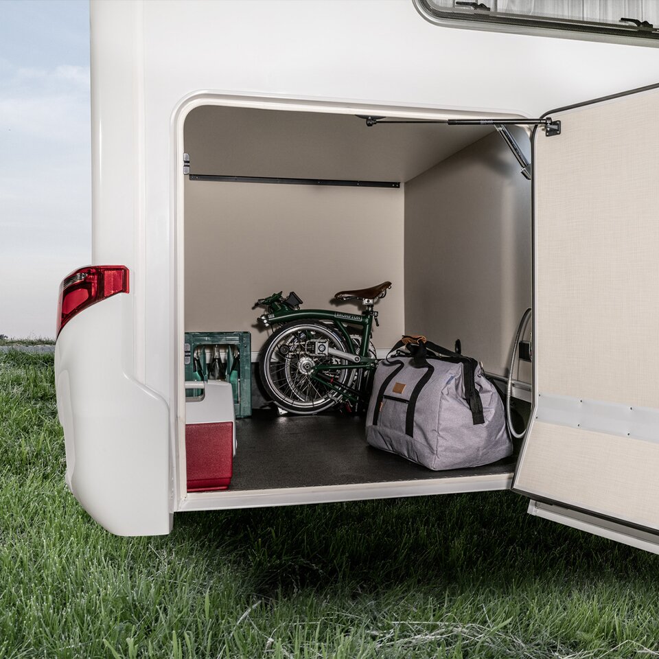 In the open garage of the HYMER Tramp S, a Mercedes Sprinter camper van, there is a travel bag, a folding bike, a drinks crate and accessory cases.