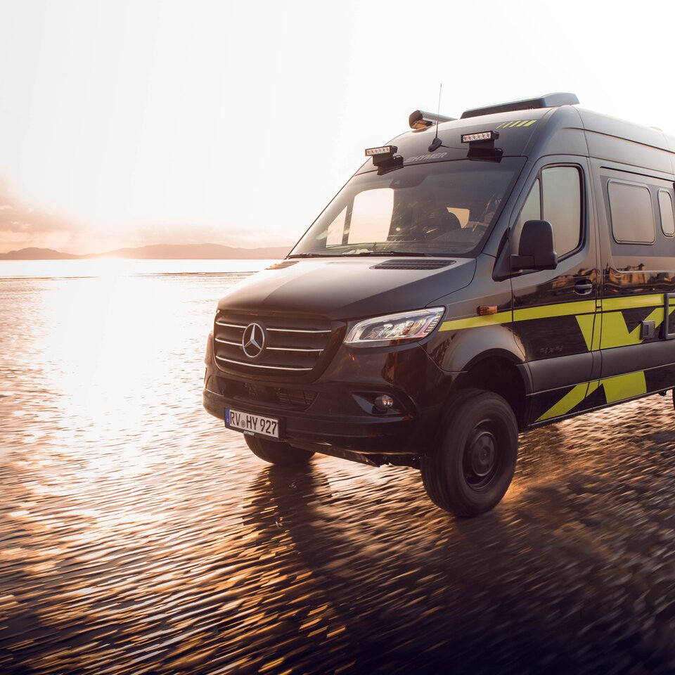 The HYMER Grand Canyon S Mercedes all-wheel drive campervan is travelling fast on a sunny, wet beach. The surroundings are blurred due to the dynamics.