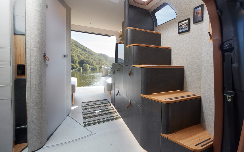 View of the stairs in the VisionVenture concept vehicle in gray and wood look, with drawers under the steps in the Mercedes camper, the rear is open.