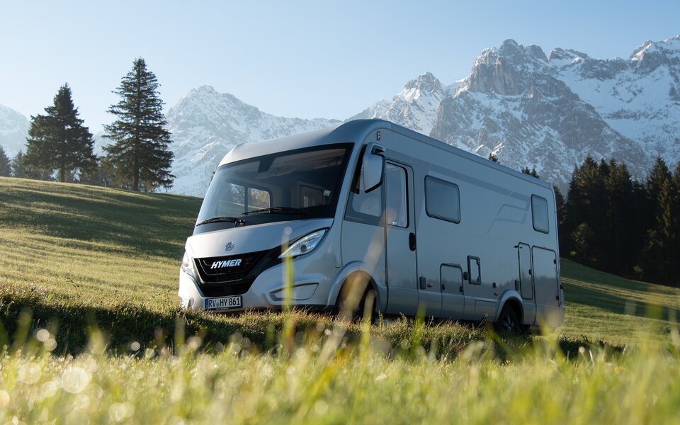 HYMER B ModernComfort in a meadow with snow-capped mountains and blue sky