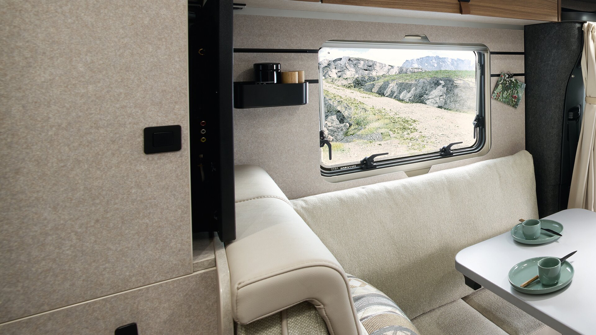 The TV in the seating area of the HYMER ML-T in the Velvet Ash style world flushes with the wall. The modern headrests are visible.