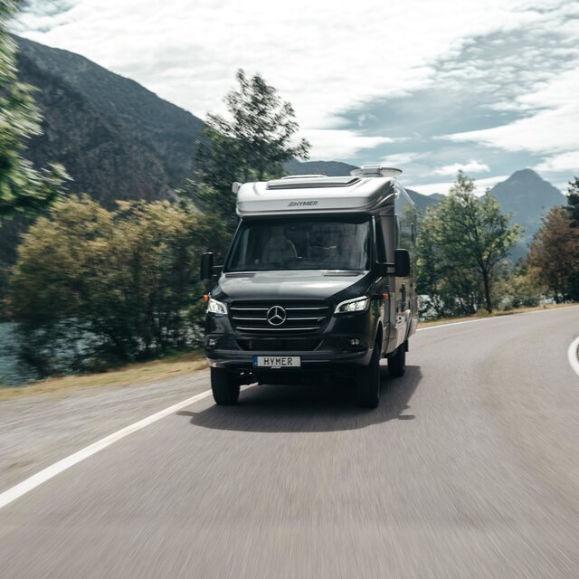 The HYMER ML-T is seen head-on, navigating a curve. The surroundings are blurred due to motion.
