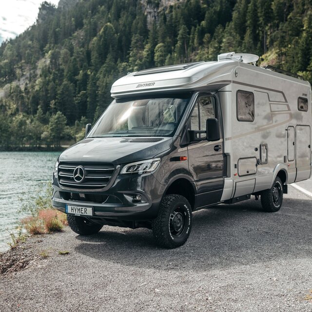 The HYMER ML-T is seen head-on, standing in front of a mountain lake.