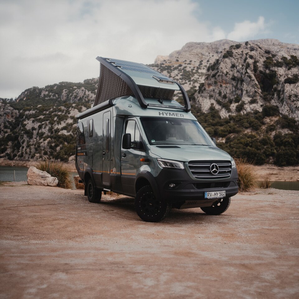 View from the rear side of the Venture S, with the pop-top and Sunset Deck extended, mountains and water in the background.