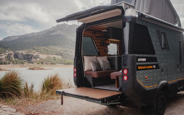 View from the rear side of the Venture S, with the pop-top and Sunset Deck extended, mountains and water in the background.