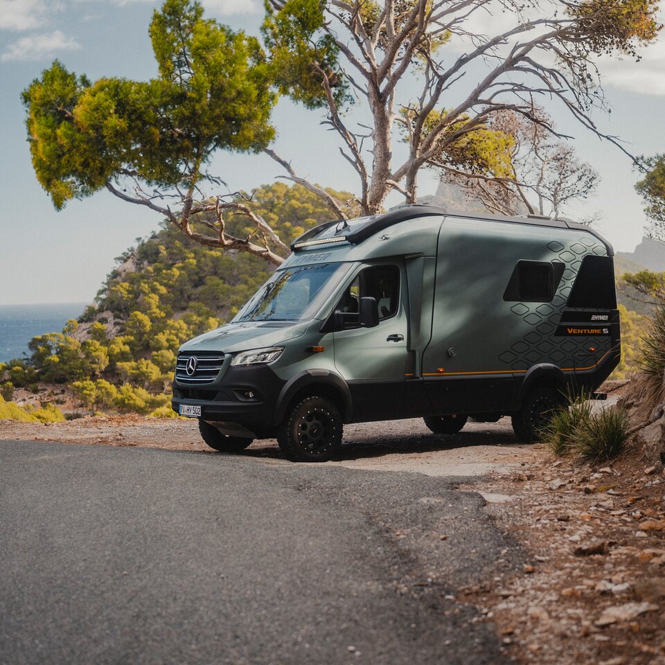 View from the front side of the Venture S, parked by the roadside, surrounded by mountains, trees, and the sea.