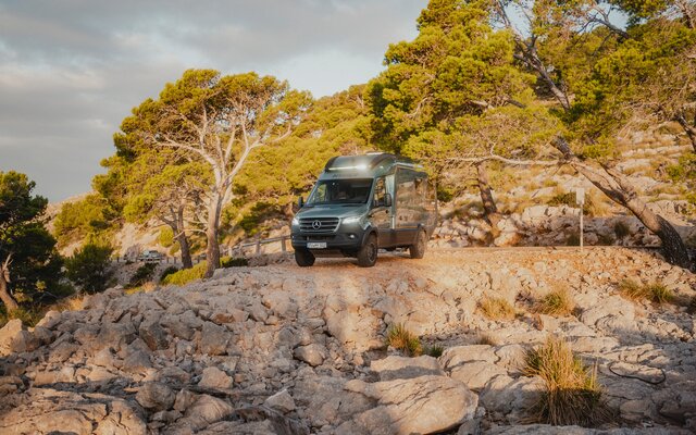 View from the front of the Venture S, headlights on, the vehicle is standing in front of a rocky abyss, surrounded by trees.
