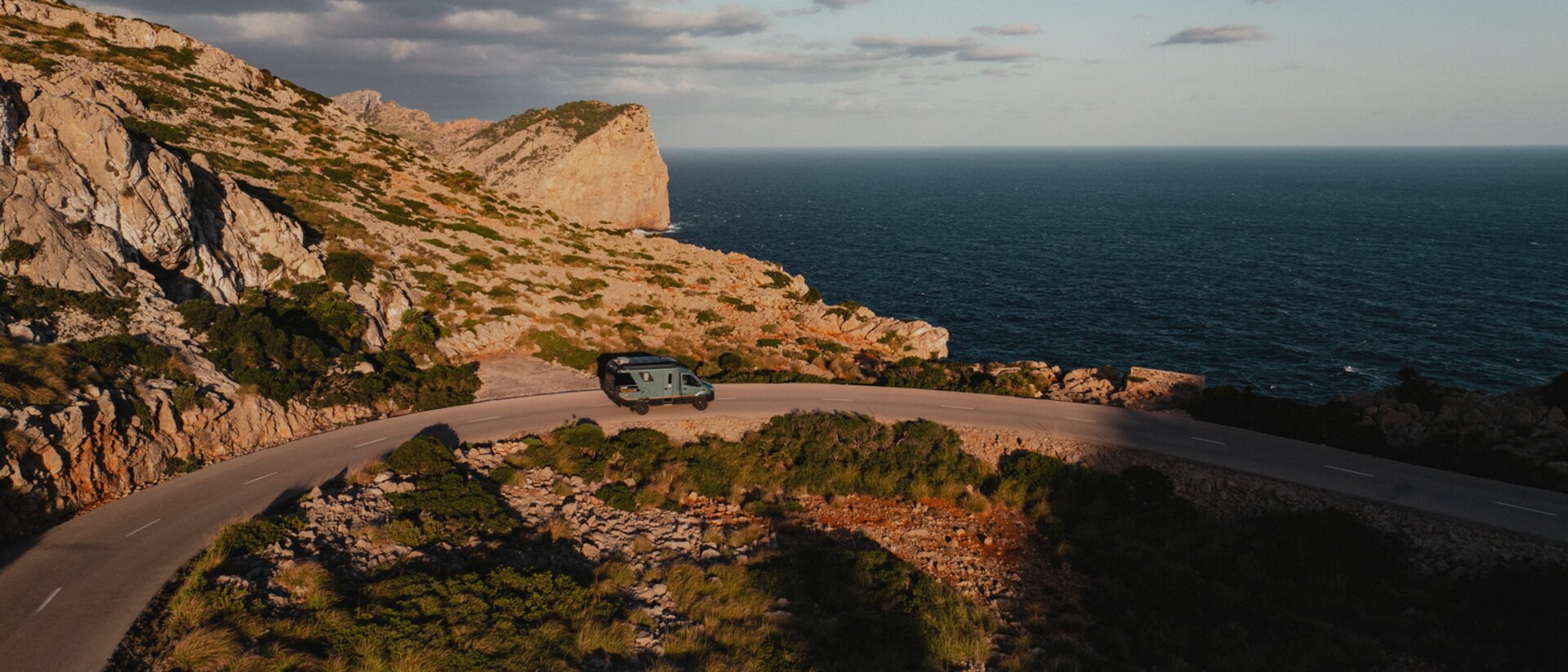 Aerial view of the Venture S driving down winding roads, with mountains and the sea in the background.