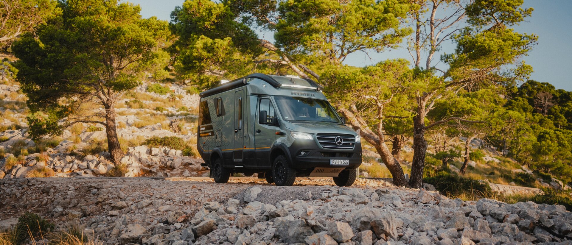 View from the front side of the Venture S, headlights on, standing in front of a rocky abyss, surrounded by trees.