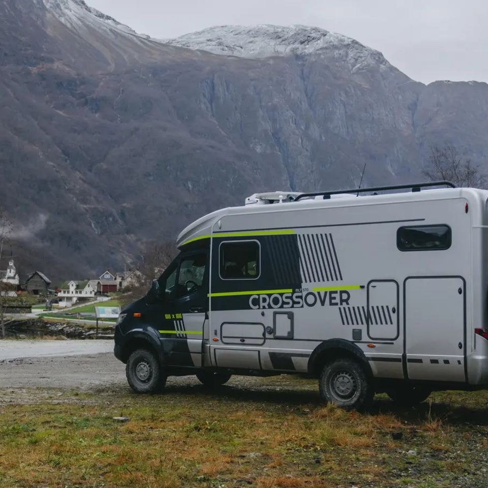 Sideudsigt af førersiden af HYMER ML-T CrossOver, køretøjet er parkeret, store bjerge med enorme klippevægge i baggrunden