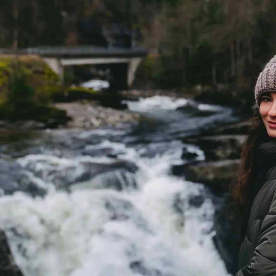 Udsigt over en kvinde, en flod med et lille vandfald i baggrunden