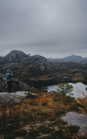 Udsigt bagfra af en mand, der tager et foto af en sø, søen omgivet af et klippefyldt landskab