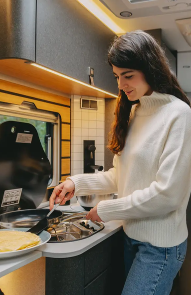 Ung kvinde, der tilbereder pandekager i autocamperkøkkenet i en meget moderne autocamper