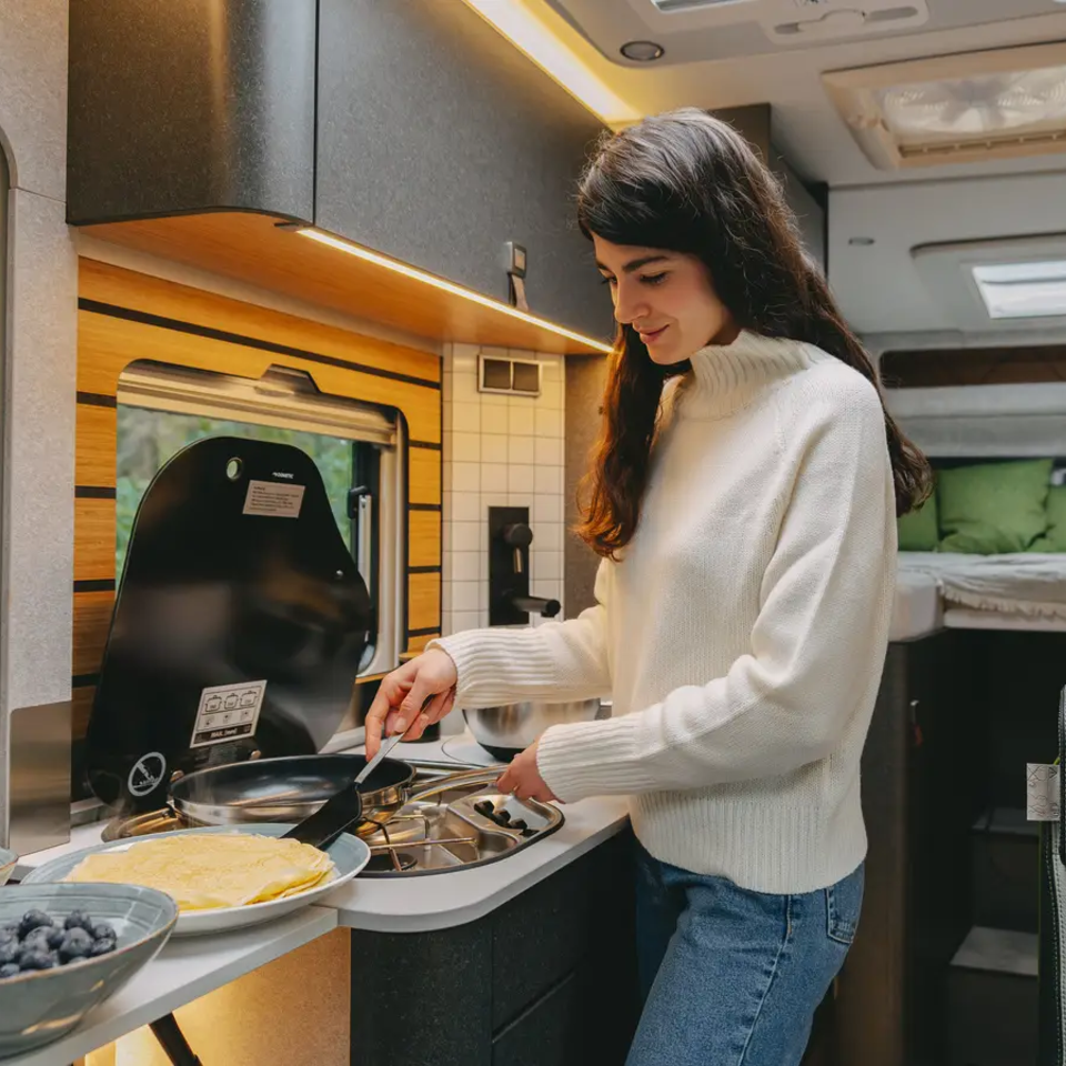 Jeune femme préparant des crêpes dans la cuisine d'un camping-car très moderne