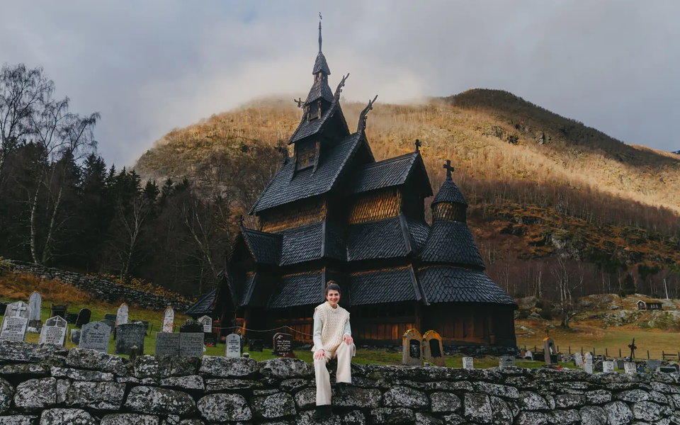 Udsigt over en kvinde, der sidder på en stenmur, Borgund stavkirke er i baggrunden