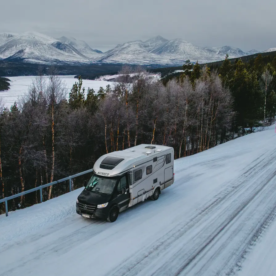 Udsigt over HYMER B-MC, parkeret på en sneklædt vej, sneklædte bjerge i baggrunden