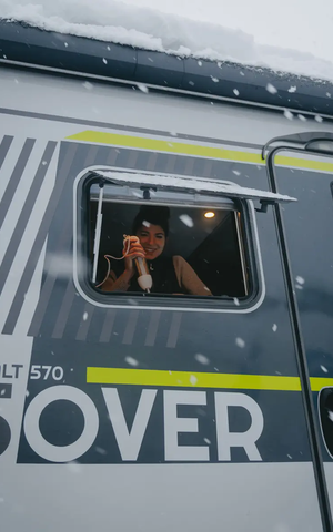 Udsigt fra passagersiden udenfor ind i køkkenvinduet på HYMER ML-T 570 CrossOver, en kvinde ses i vinduet