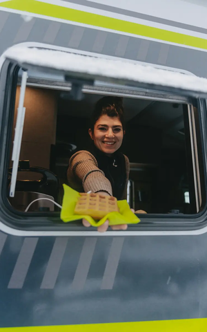Udsigt ind i køkkenvinduet på HYMER ML-T 570 CrossOver, en kvinde rækker en vaffel ud